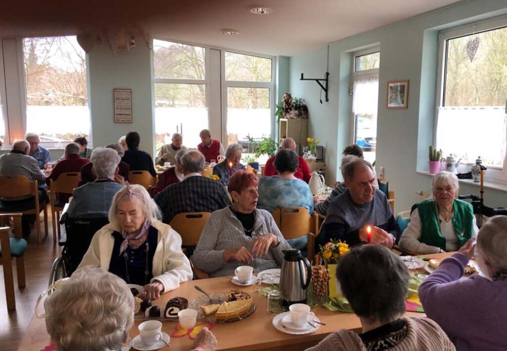 Personen sitzen an Tischen in einem hell erleuchteten Raum und nehmen an einem sozialen Treffen teil.