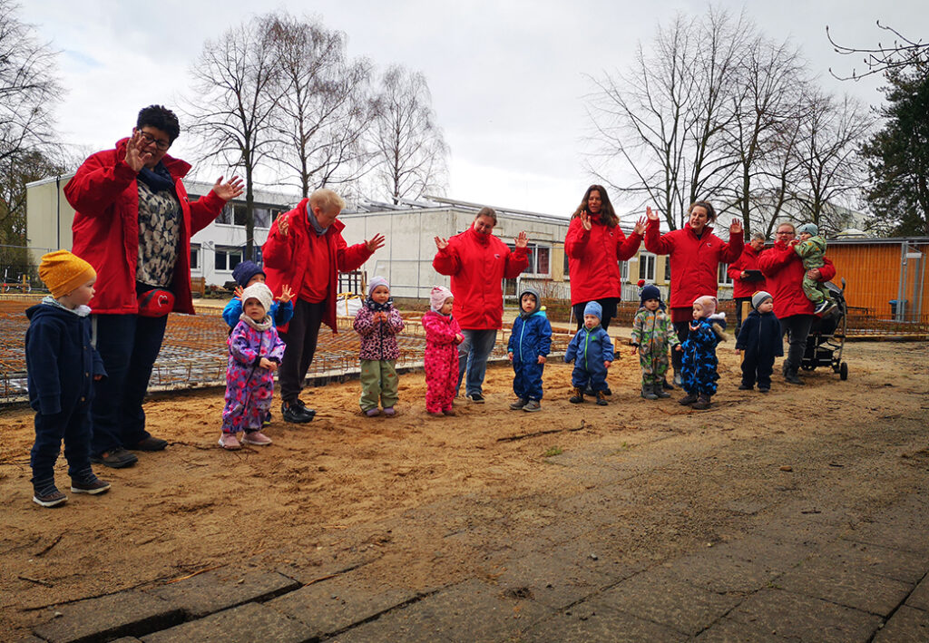 Erzieherinnen und Kinder in einer Reihe im Freien bei einem Kindergartenausflug.