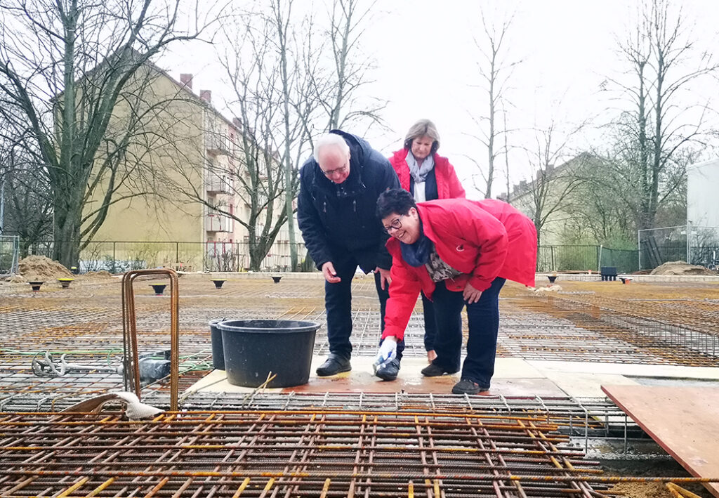 Drei Personen bei einer Grundsteinlegung auf einer Baustelle.