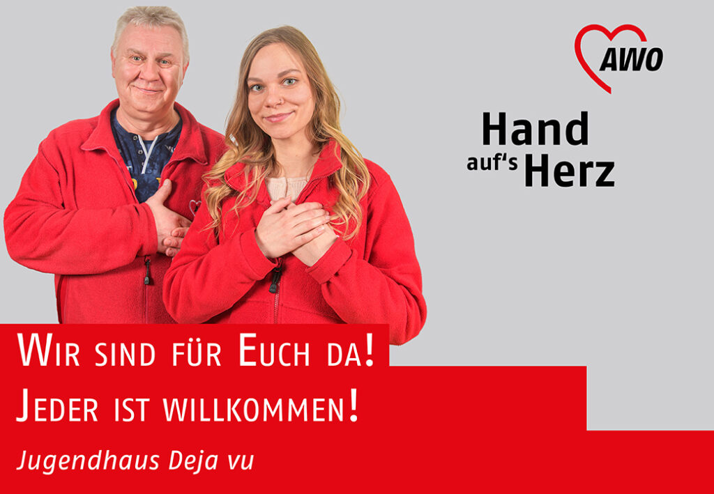 Zwei Personen in roten Jacken mit Hand aufs Herz-Geste vor einem AWO-Logo.