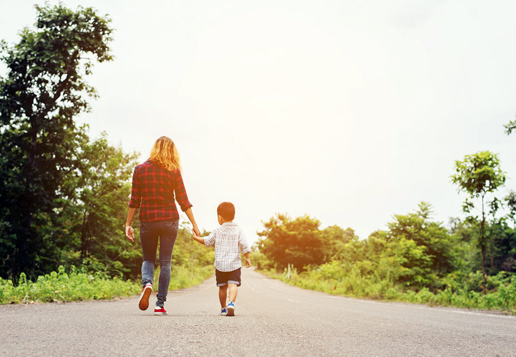 Eine Frau und ein Kind Hand in Hand auf einer Landstraße
