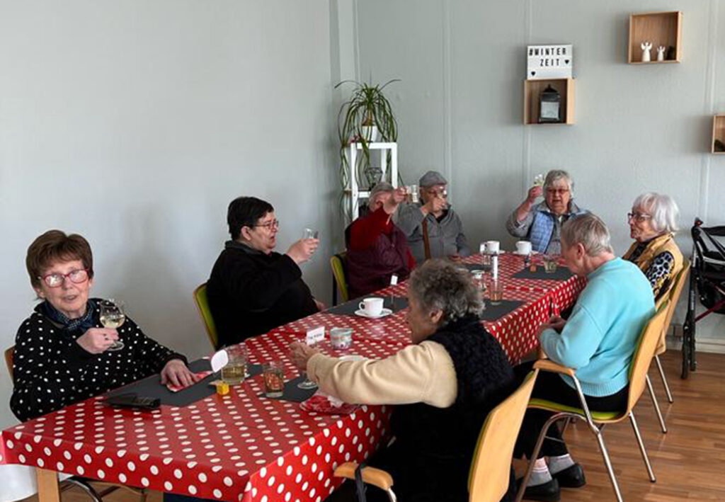&Auml;ltere Damen sitzen um einen Tisch mit rot-wei&szlig; gepunkteter Tischdecke und heben Gl&auml;ser zum Ansto&szlig;en.
