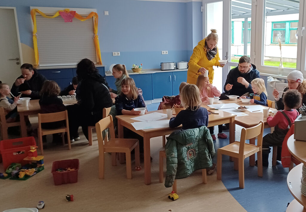 Eine Gruppe von Erwachsenen und Kindern in einem Gemeinschaftsraum, die gemeinsam essen.