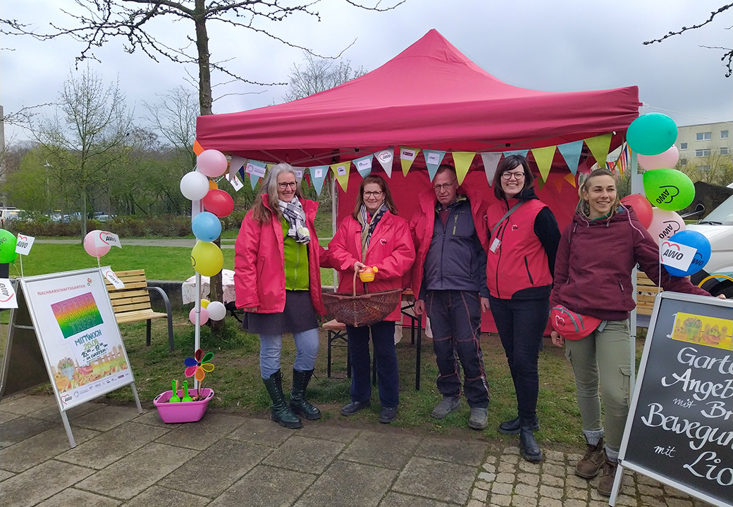 Gruppenbild von fünf Personen in pinken Jacken vor einem roten Pavillon mit bunten Ballons und Bannern.