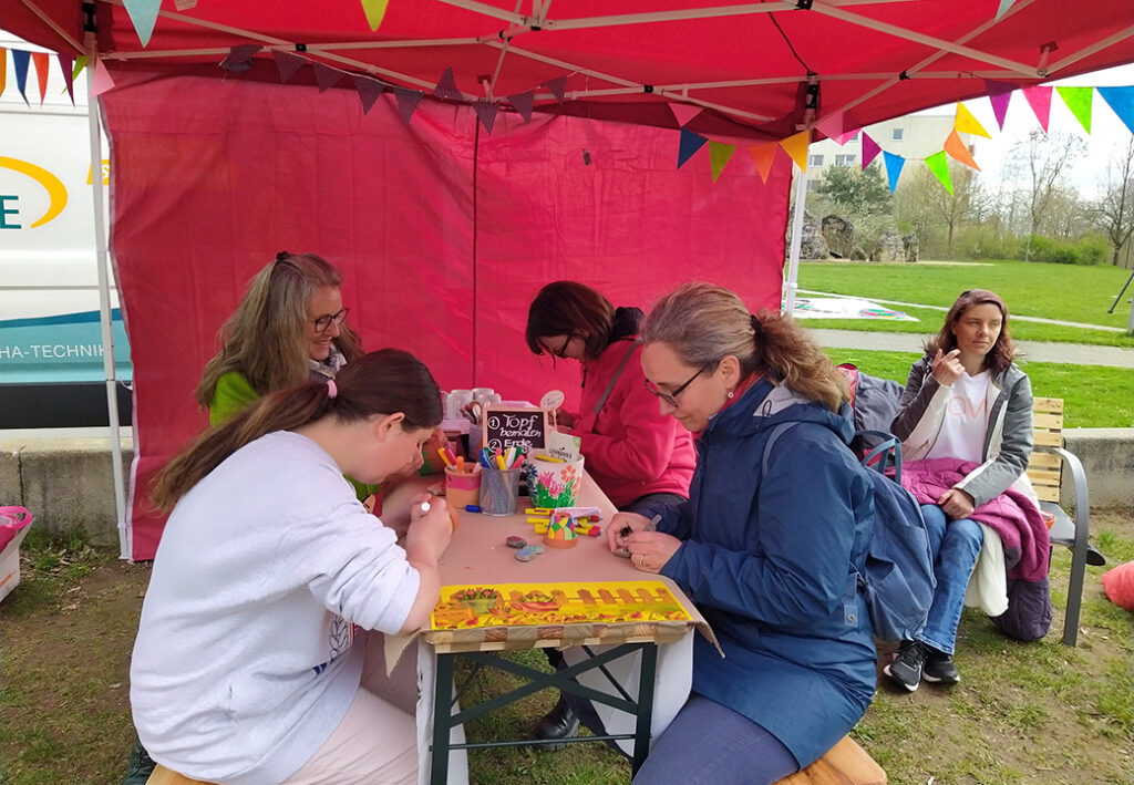 Personen, die unter einem rot-wei&szlig;en Pavillon an einem Tisch sitzen und basteln.
