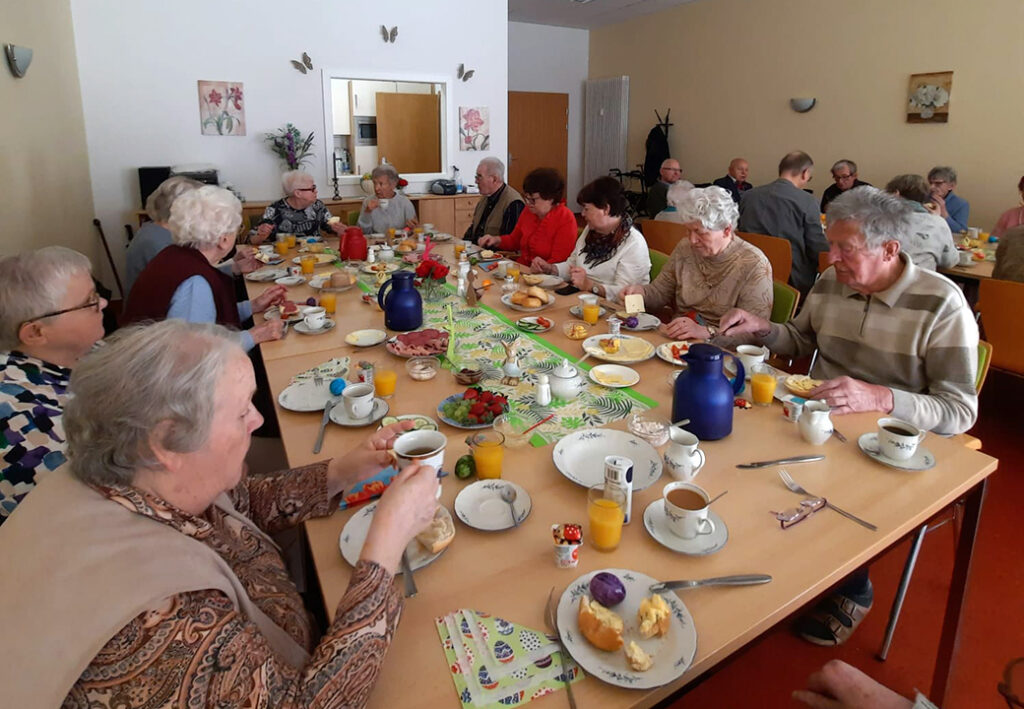 Eine Gruppe &auml;lterer Menschen sitzt gemeinsam an einem Esstisch und genie&szlig;t eine Mahlzeit.