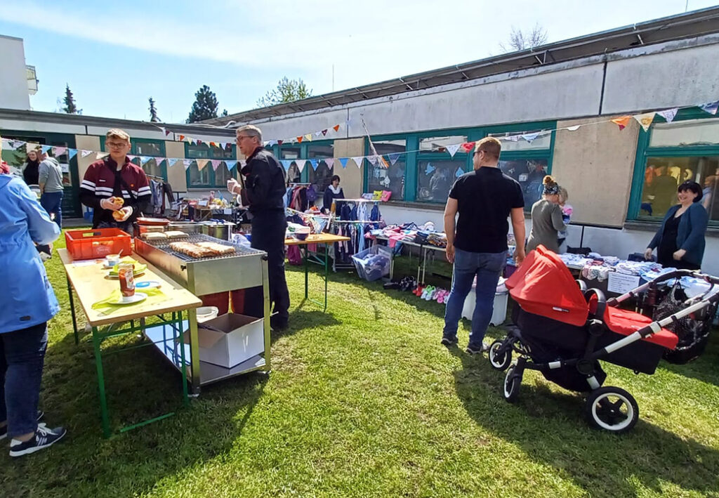 Menschen bei einem Freiluft-Flohmarkt, einige stehen an einem Grillstand.