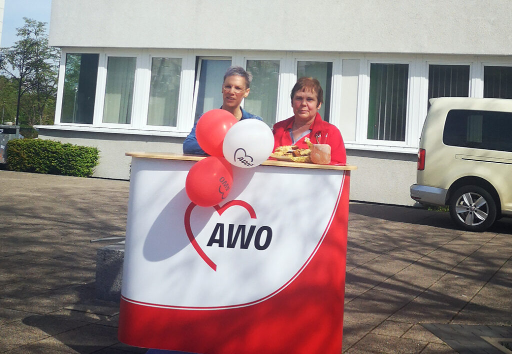 Zwei Personen stehen hinter einem AWO-Promotionstisch mit Luftballons.