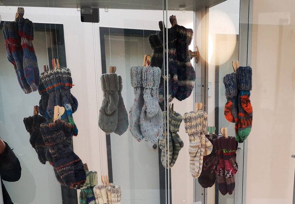 Mehrere gestrickte Handschuhe h&auml;ngen in einer Glasvitrine.
