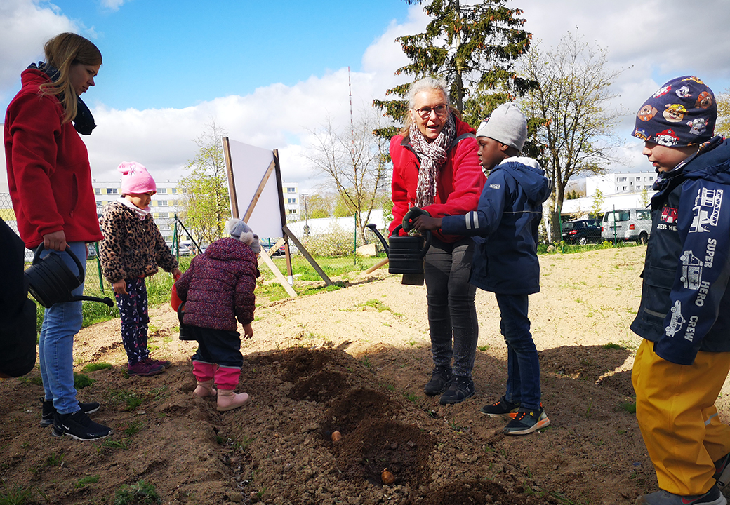 Mehrere Menschen, darunter Kinder und ein Erwachsener, bepflanzen ein Beet im Freien.