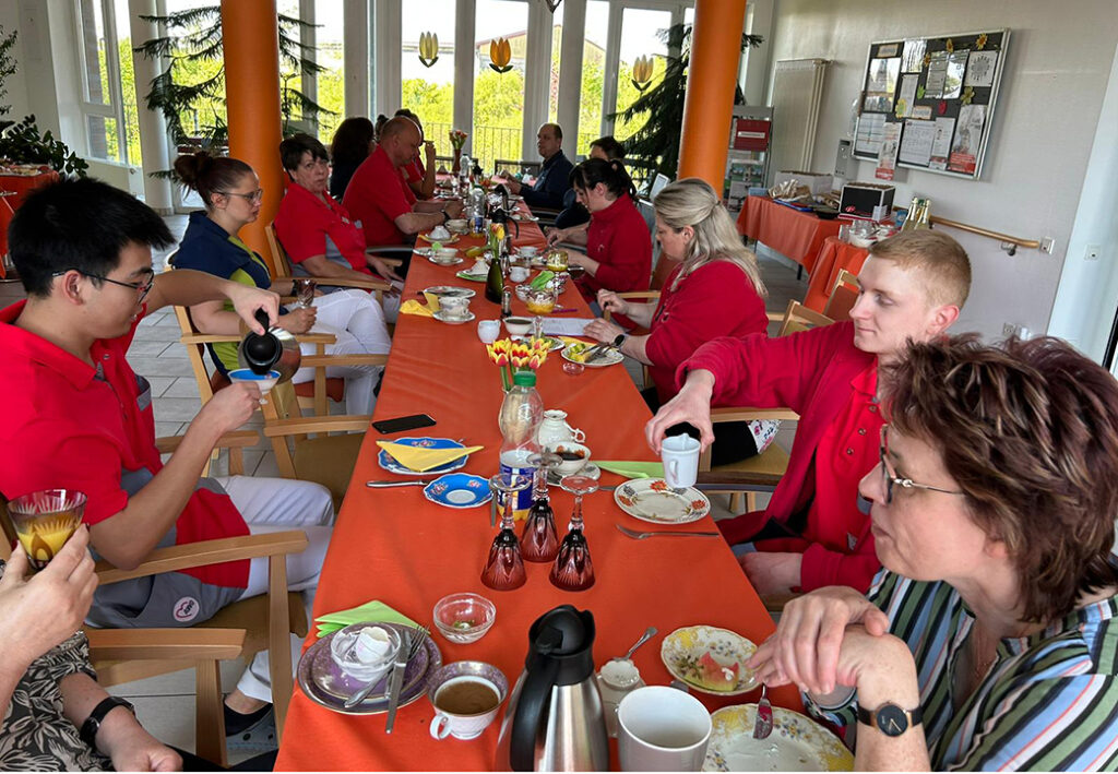 Eine Gruppe von Menschen in roter Kleidung sitzt an einem langen Tisch und unterhält sich während eines gemeinsamen Essens.