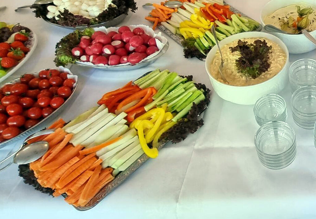 Vegetable platter with various dips and glasses on a table.