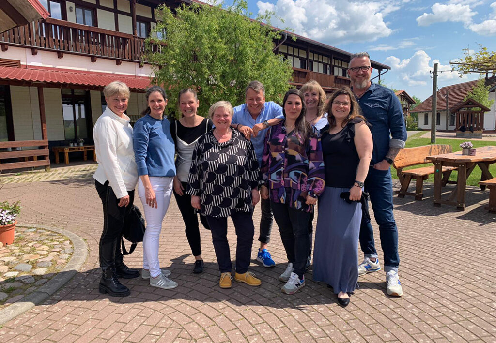 Gruppe von neun Personen posiert lächelnd im Freien vor einem Gebäude.