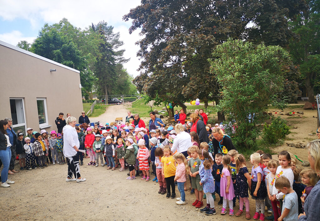 Gruppe von Kindern und Erwachsenen versammelt im Freien vor einem Geb&auml;ude.