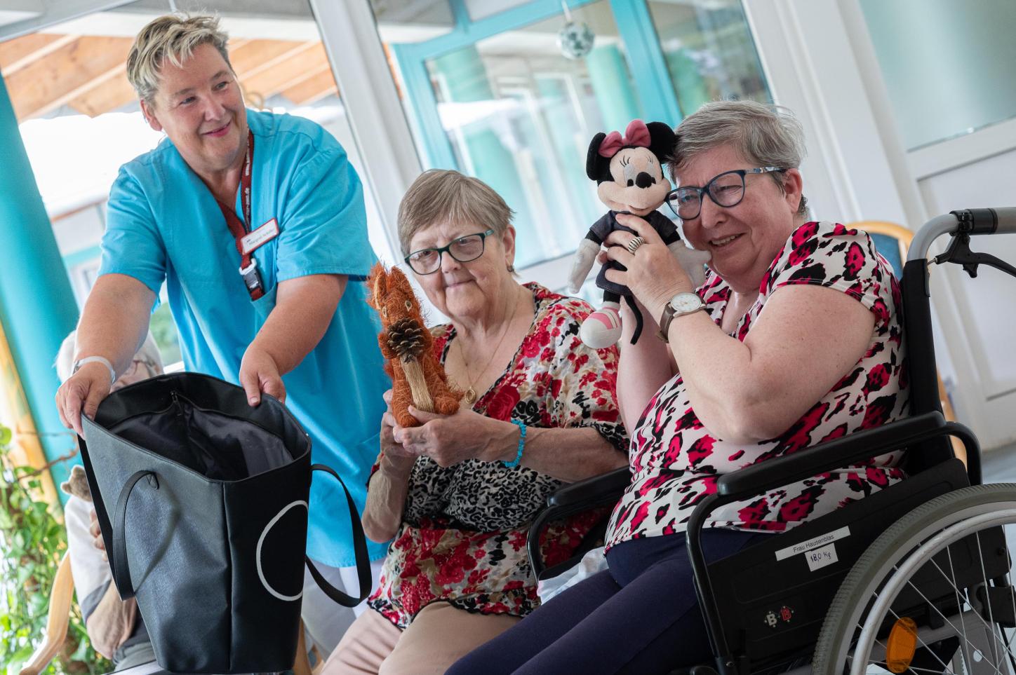 Pflegekraft mit zwei älteren Damen, die Stofftiere halten