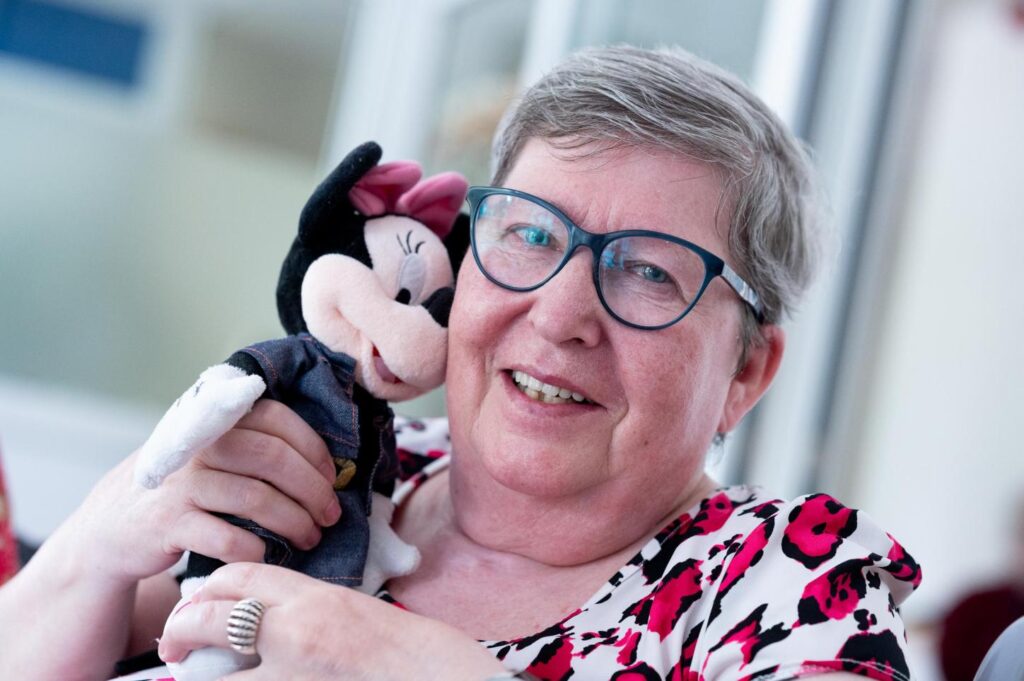 Eine l&auml;chelnde Frau mit Brille h&auml;lt ein Pl&uuml;schtier in der Hand.