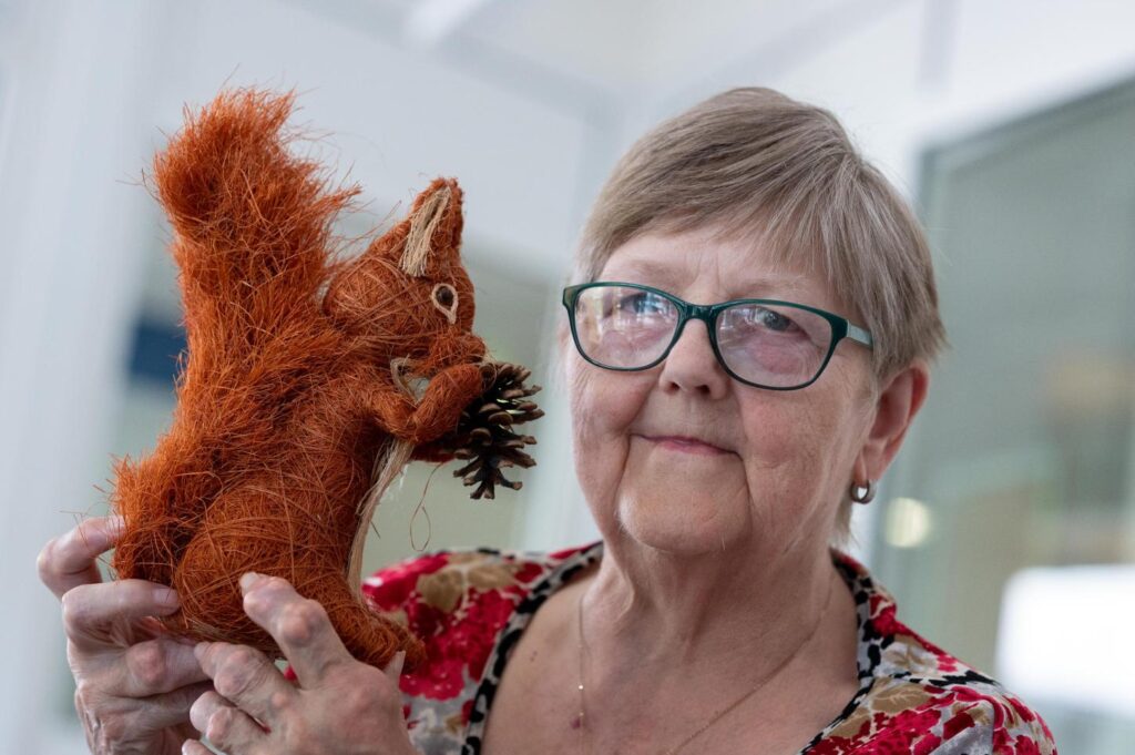 Eine &auml;ltere Frau mit Brille h&auml;lt eine k&uuml;nstliche Eichh&ouml;rnchenfigur.