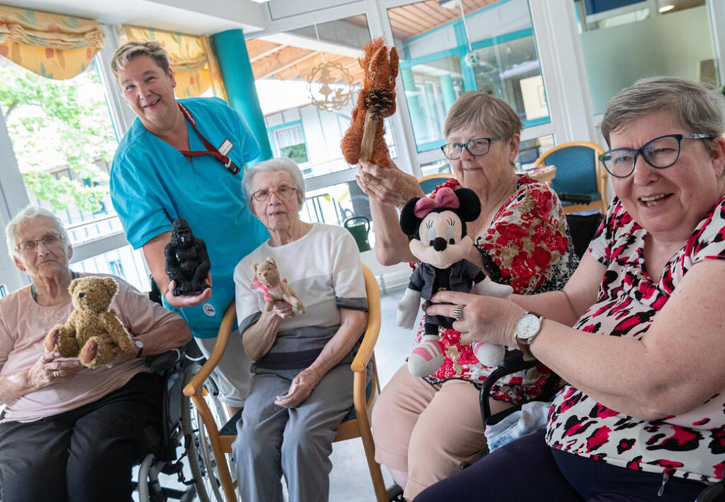Gruppe von Senioren und einer Betreuerin, die Stofftiere halten.
