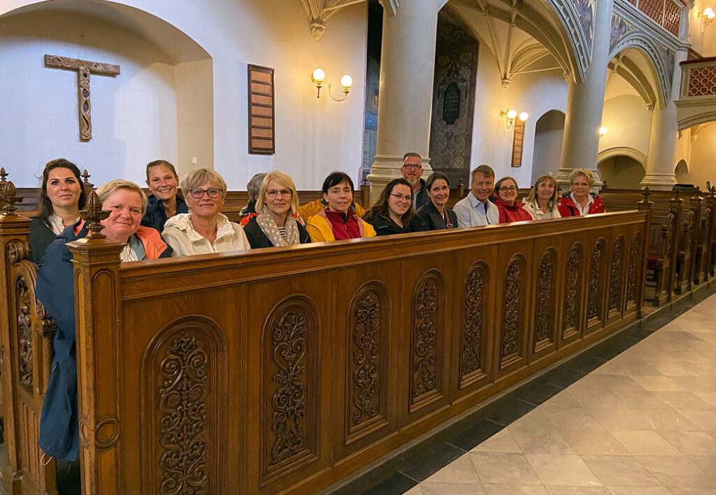 Eine Gruppe von Menschen sitzt in einer Kirchenbank in einem historischen Geb&auml;ude.