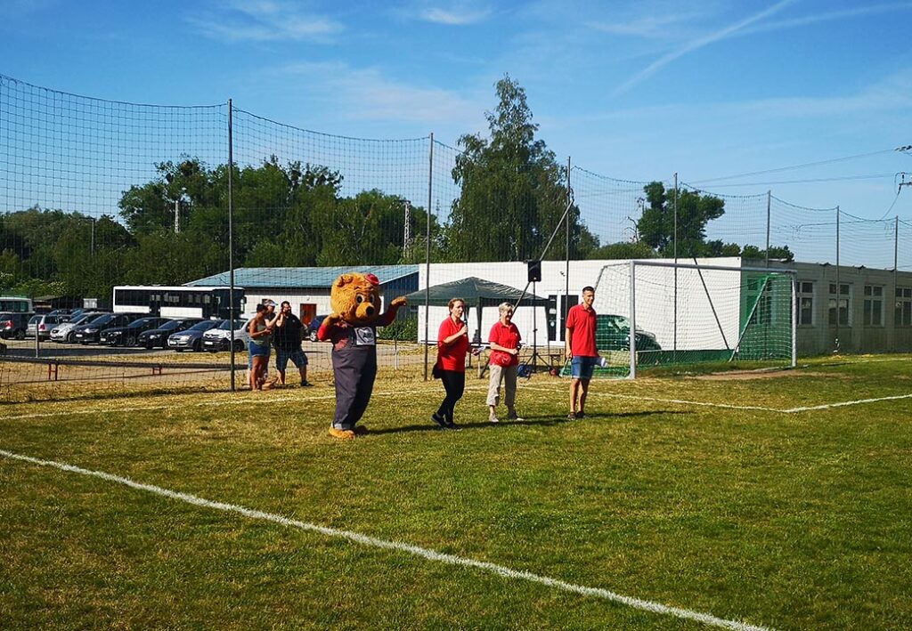 Menschen auf einem Fußballfeld mit einem Maskottchenbär