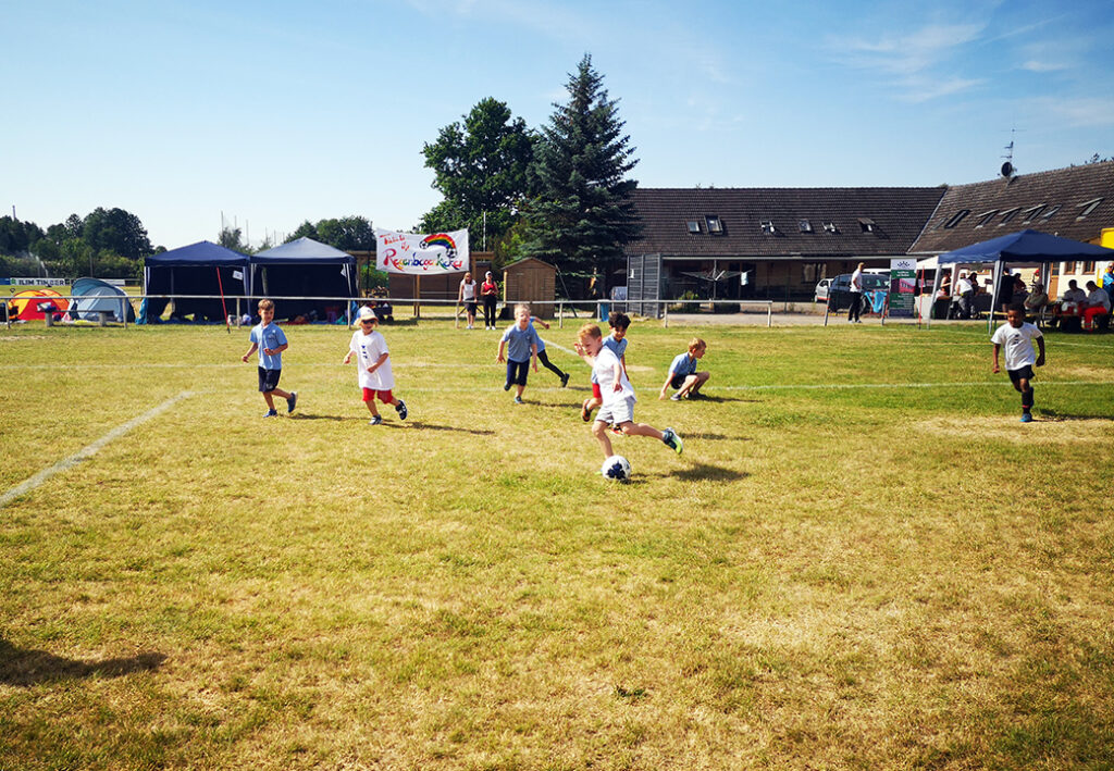 Kinder spielen Fu&szlig;ball auf einer Wiese, mehrere Zelte im Hintergrund