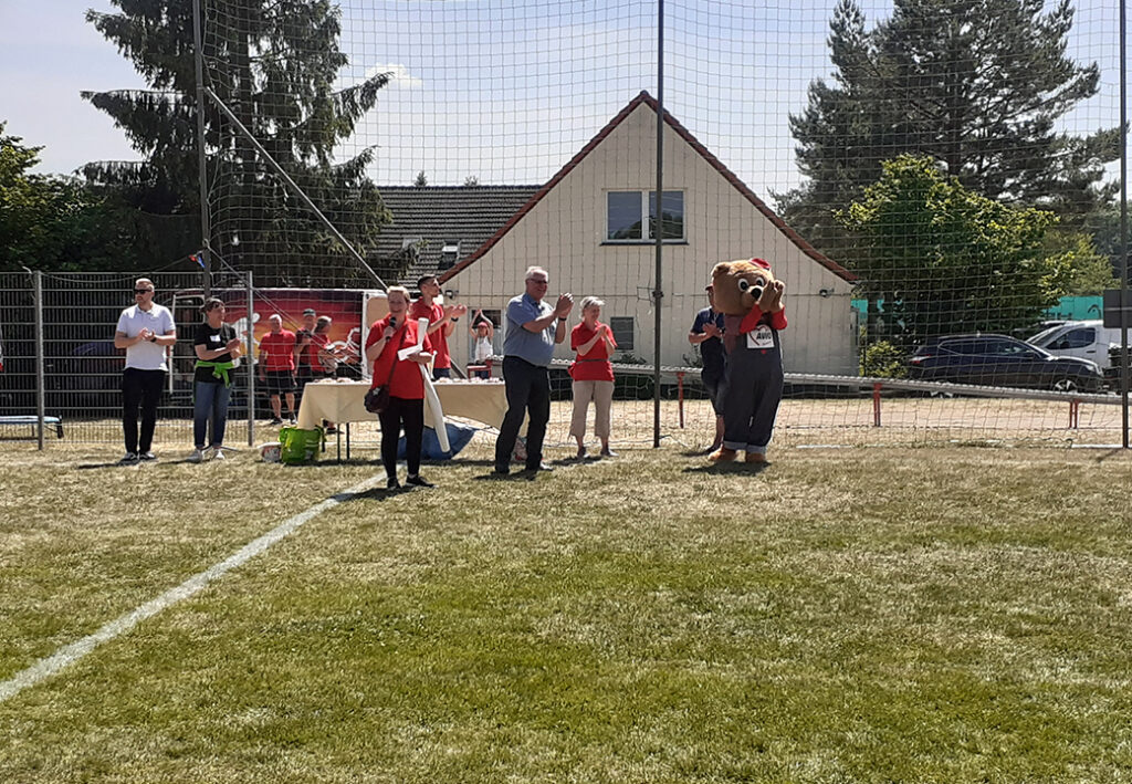 Personen bei einem Outdoor-Event hinter einem Zaun, einige tragen AWO-T-Shirts, eine Person ist im B&auml;renkost&uuml;m.