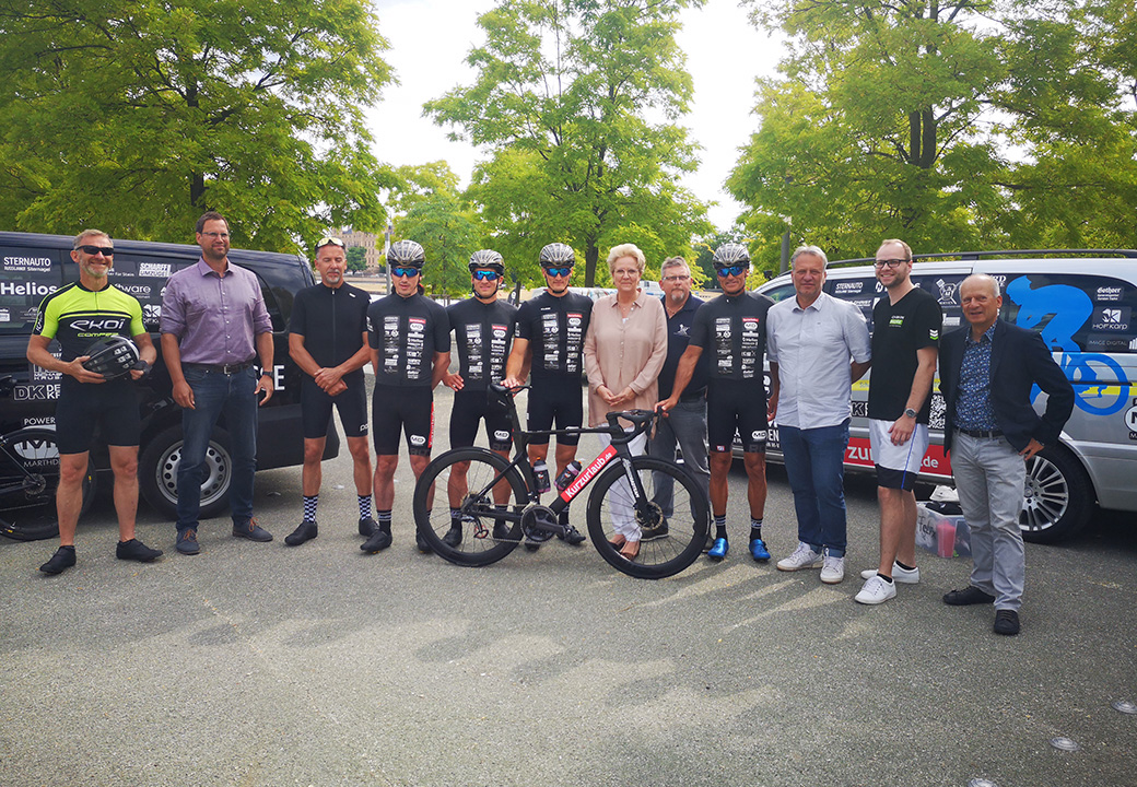 Gruppe von Personen mit Fahrradkleidung und Sportausrüstung vor Firmenfahrzeugen