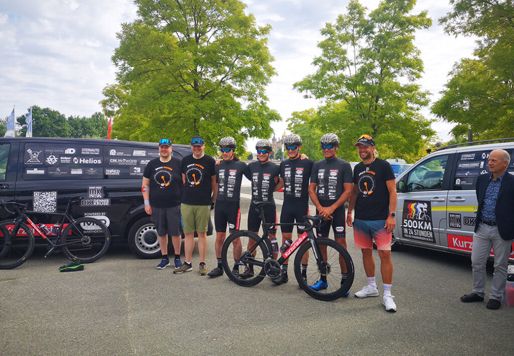 Gruppe von Radfahrern und Unterst&uuml;tzern posiert vor Fahrzeugen