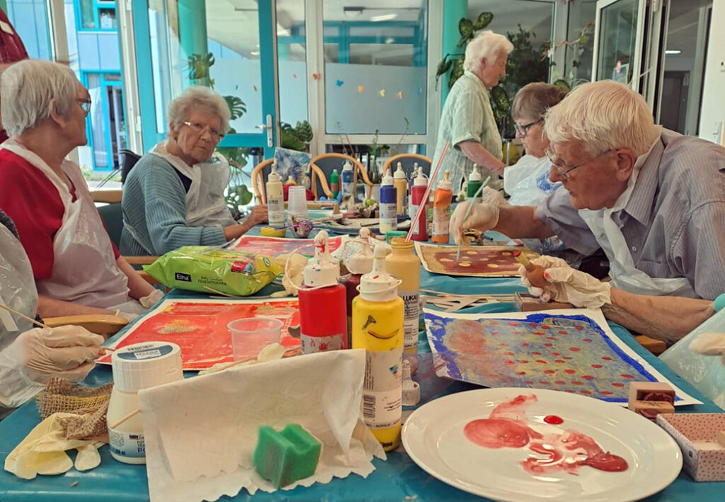 &Auml;ltere Menschen malen gemeinsam an einem Tisch.
