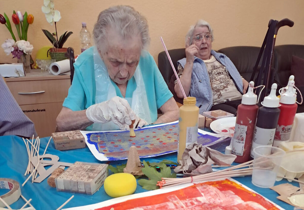 Zwei ältere Frauen, eine aktiv malend, die andere zuschauend