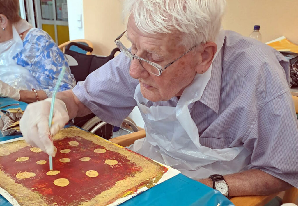 Ein &auml;lterer Mann malt an einem Tisch in einer Gemeinschaftseinrichtung.