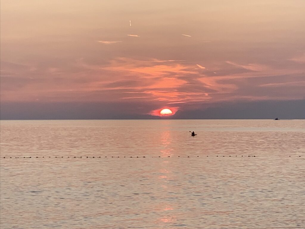 Sonnenuntergang &uuml;ber einem ruhigen Meer mit einem Boot im Vordergrund.