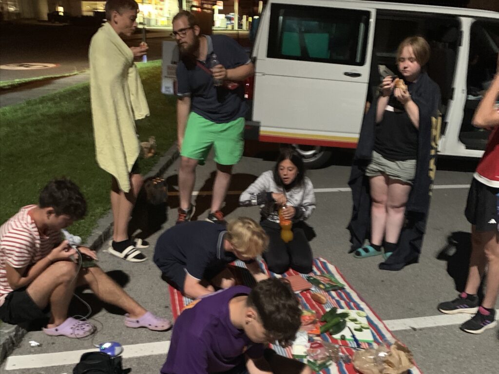 Gruppe Jugendlicher bei Nacht auf einem Parkplatz beim Picknicken