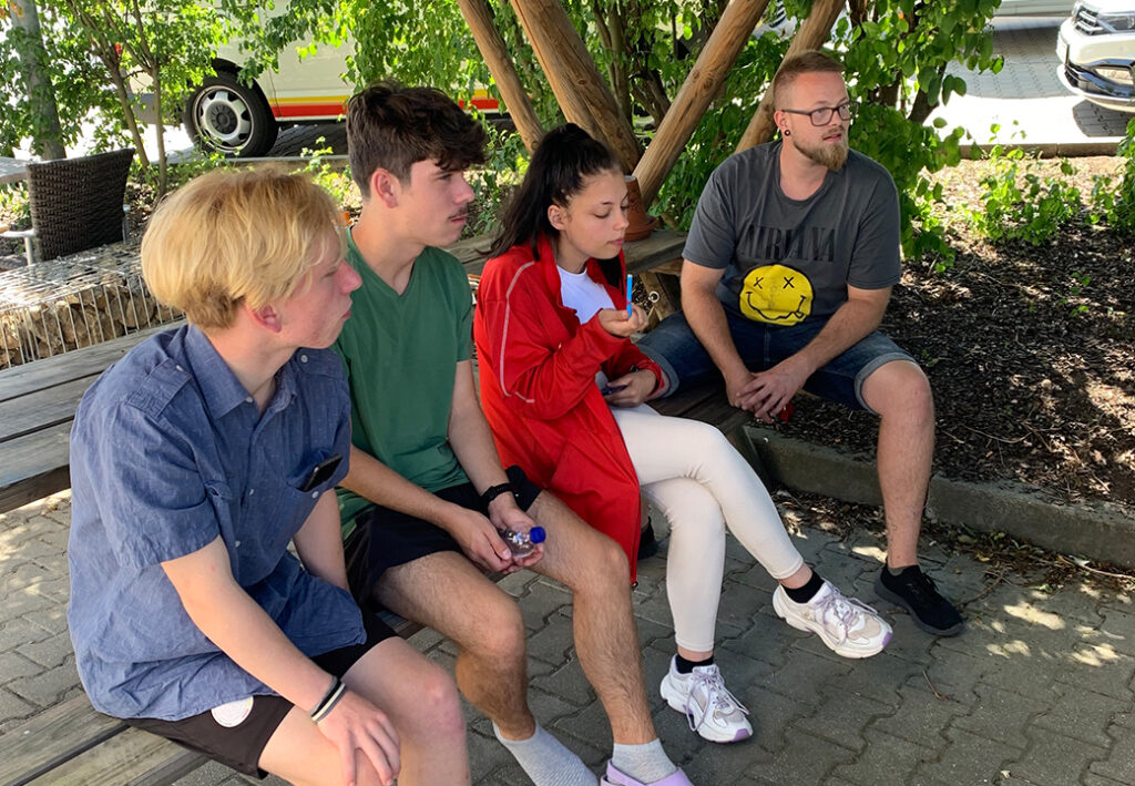 Vier Personen sitzen nebeneinander auf einer Bank im Freien.