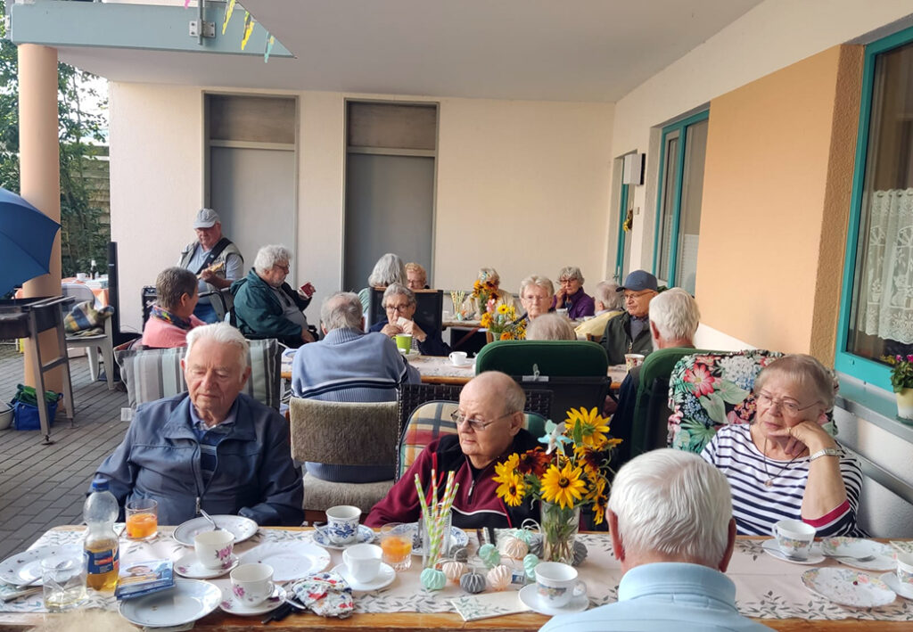 &Auml;ltere Menschen sitzen an einem gedeckten Tisch auf einer Terrasse.