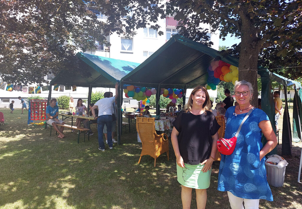 Zwei Frauen bei einem Sommerfest im Freien mit Zeltdach und bunten Luftballons.
