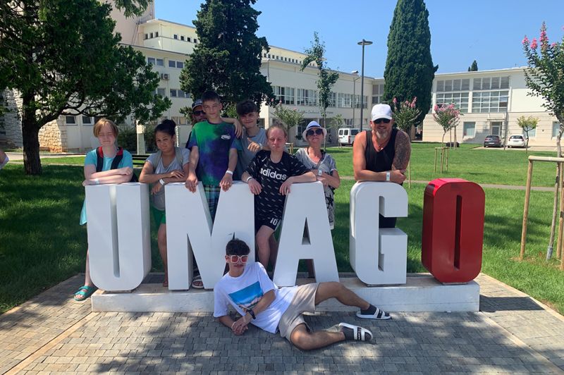 Gruppe von Menschen posiert vor dem Schriftzug 'UMAGO'.