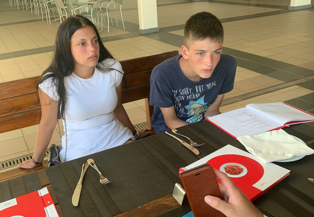 Zwei Jugendliche sitzen an einem Tisch mit einem aufgeschlagenen Men&uuml; und Tischdekoration.