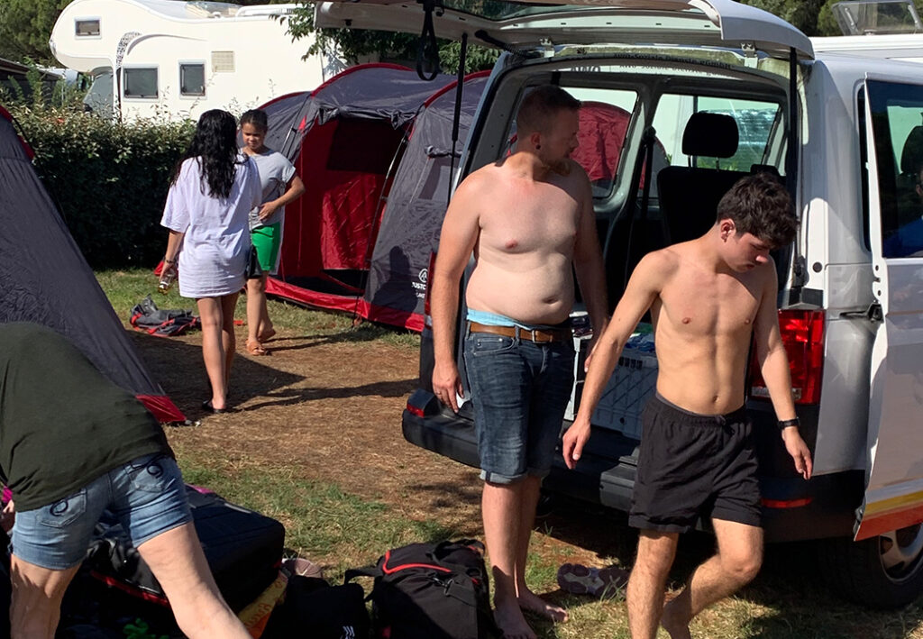 Menschen auf einem Campingplatz mit einem Van und Zelten im Hintergrund
