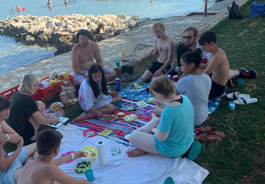 Menschen sitzen auf einer Picknickdecke am Wasser.