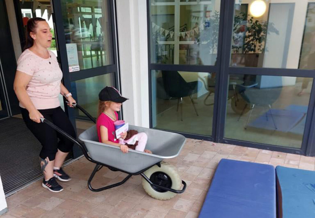 Eine Frau schiebt ein kleines M&auml;dchen in einer Schubkarre