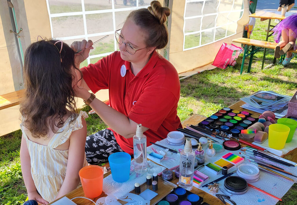 Eine Frau schminkt ein Kind in einem Zelt.