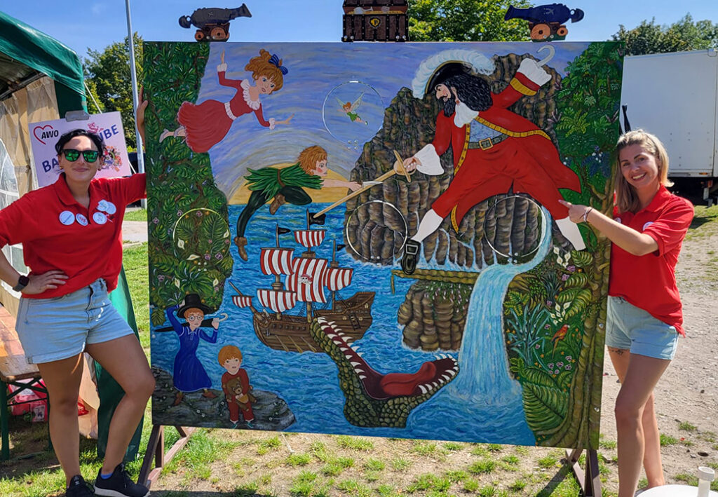 Zwei Frauen in roten T-Shirts posieren vor einem großen, bunten Gemälde.