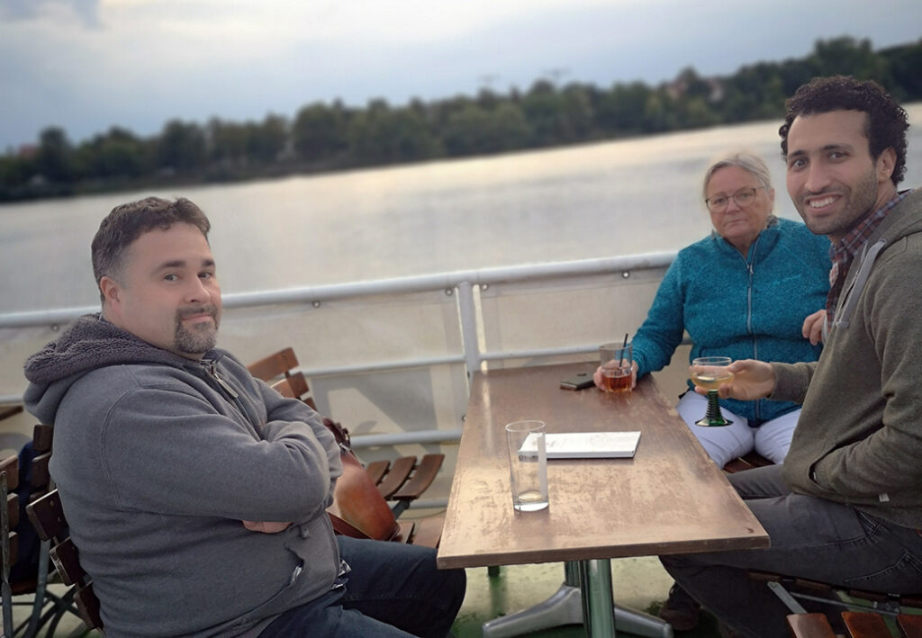 Drei Menschen sitzen an einem Tisch auf einem Boot.