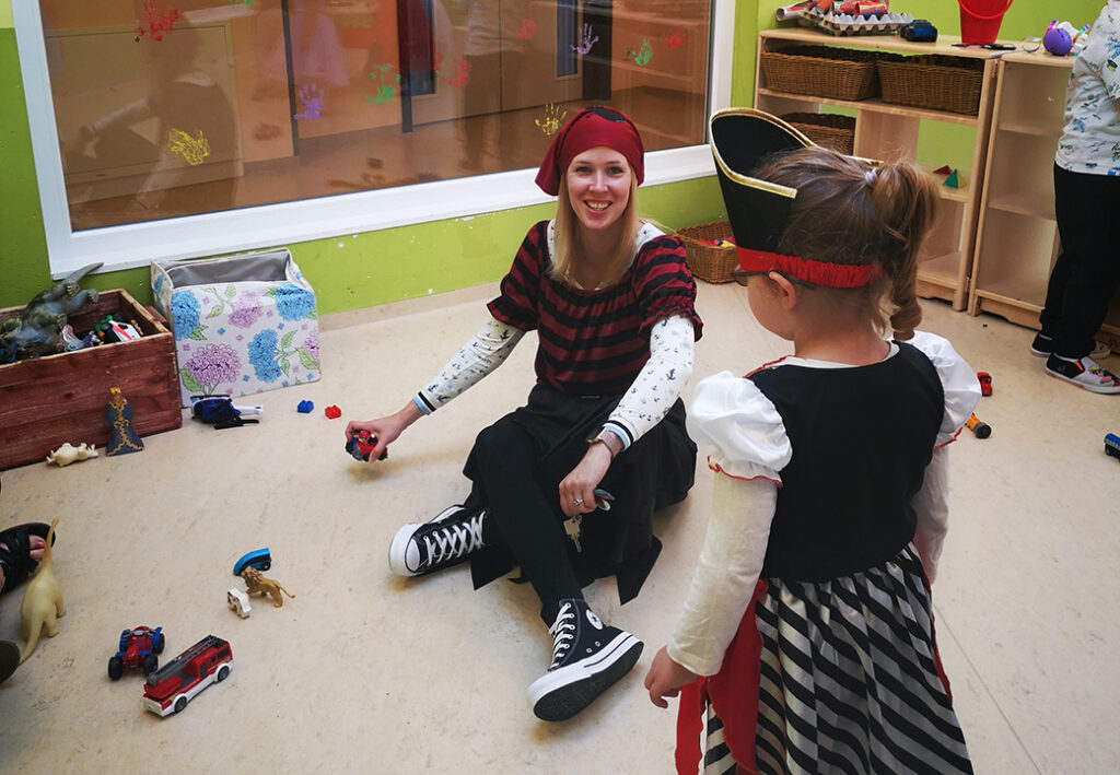 Eine Erzieherin und ein Kind spielen in einem Kindergartenzimmer, beide in Piratenkost&uuml;men.