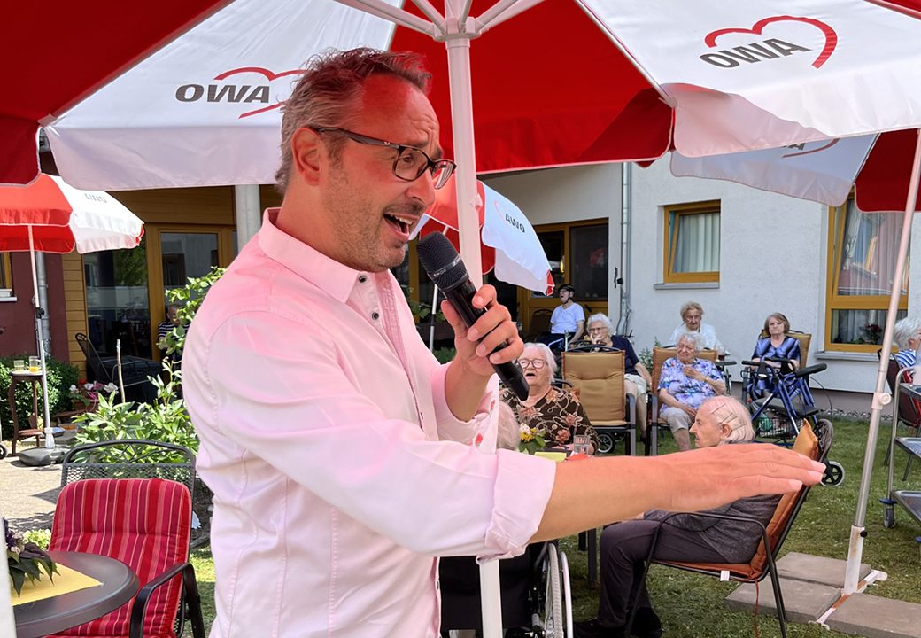 Mann singt in einem Pflegeheim der AWO unter roten Sonnenschirmen