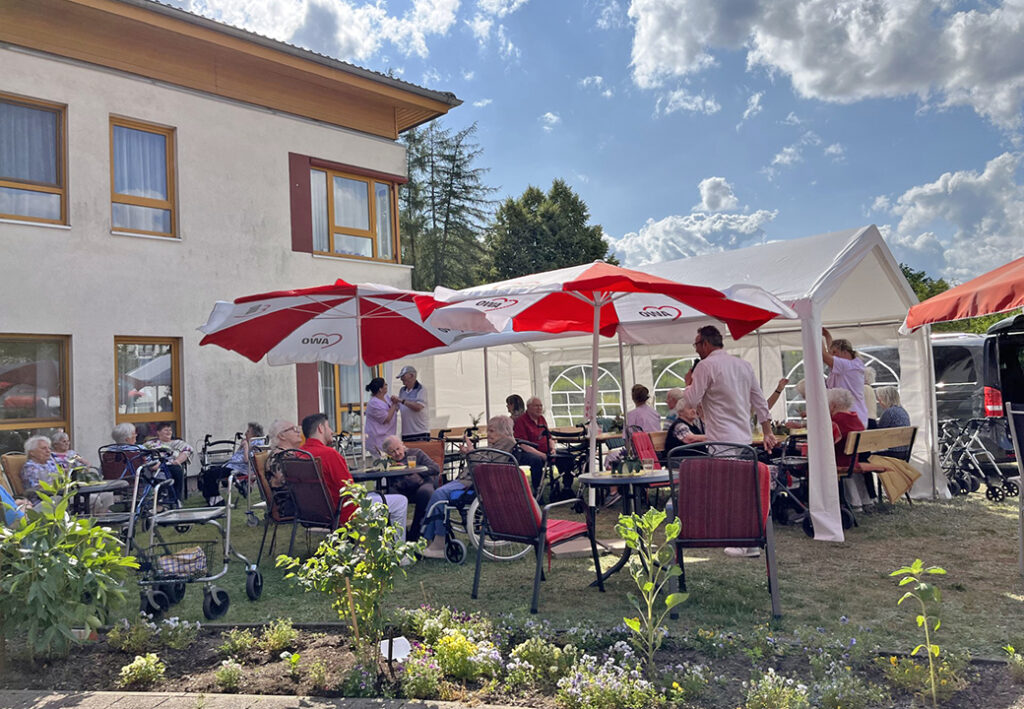 Personengruppe in einem Garten unter Sonnenschirmen und einem Pavillon