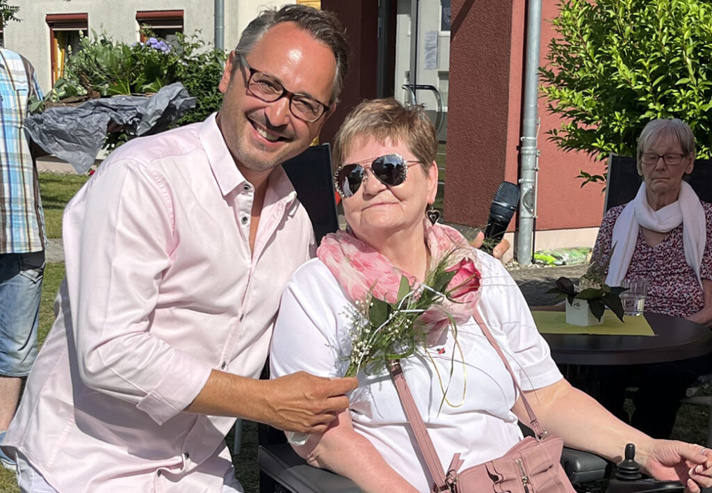 Ein Mann und eine Frau sitzen drau&szlig;en, der Mann h&auml;lt eine Blume.