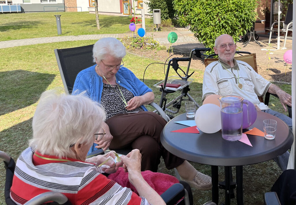&Auml;ltere Menschen sitzen in einem Garten an einem Tisch mit Dekorationen.