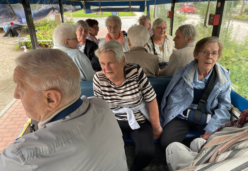 Eine Gruppe &auml;lterer Menschen sitzt in einem offenen Transportfahrzeug.